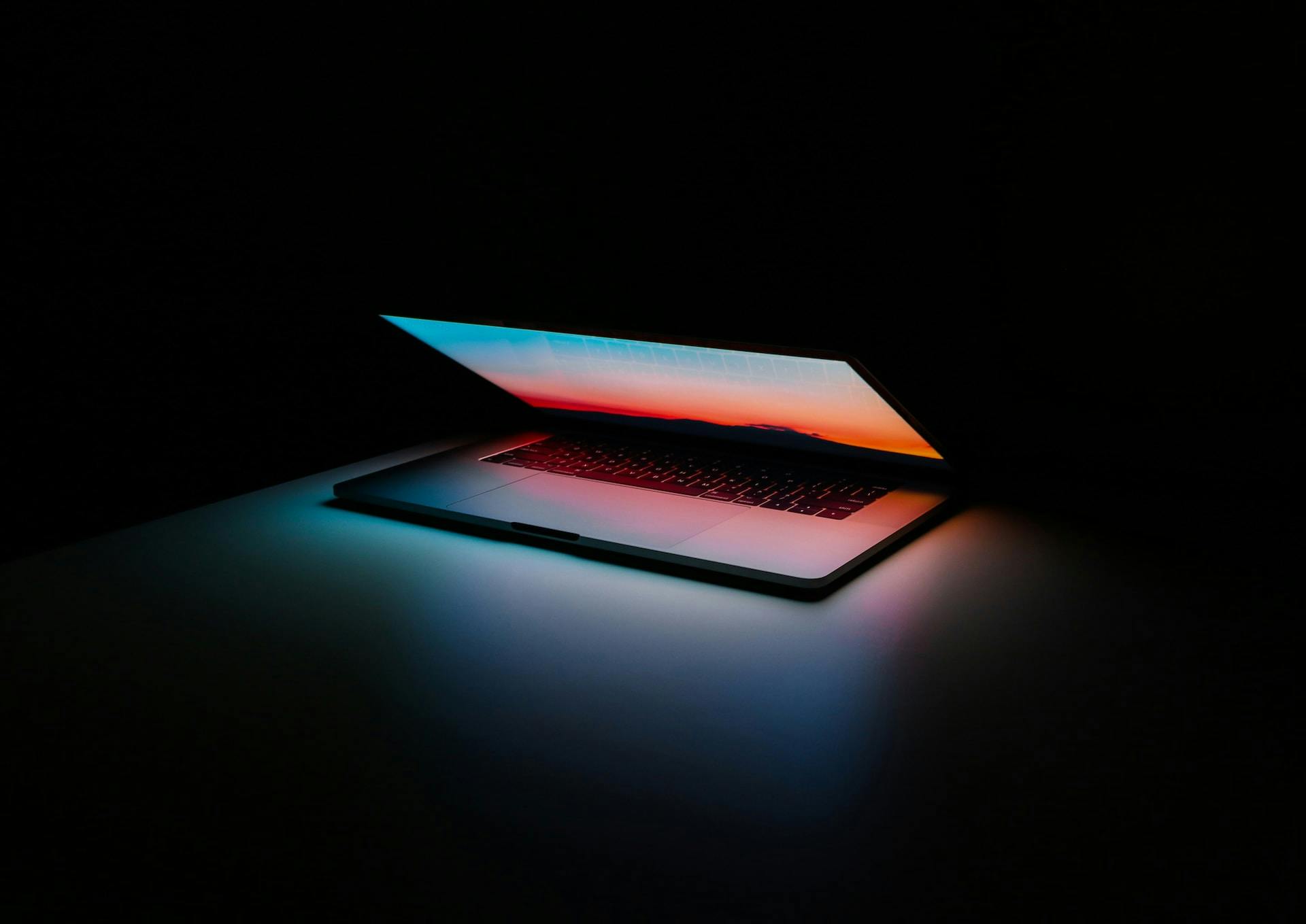 A laptop computer in a dark room with vibrant colors coming from the screen.