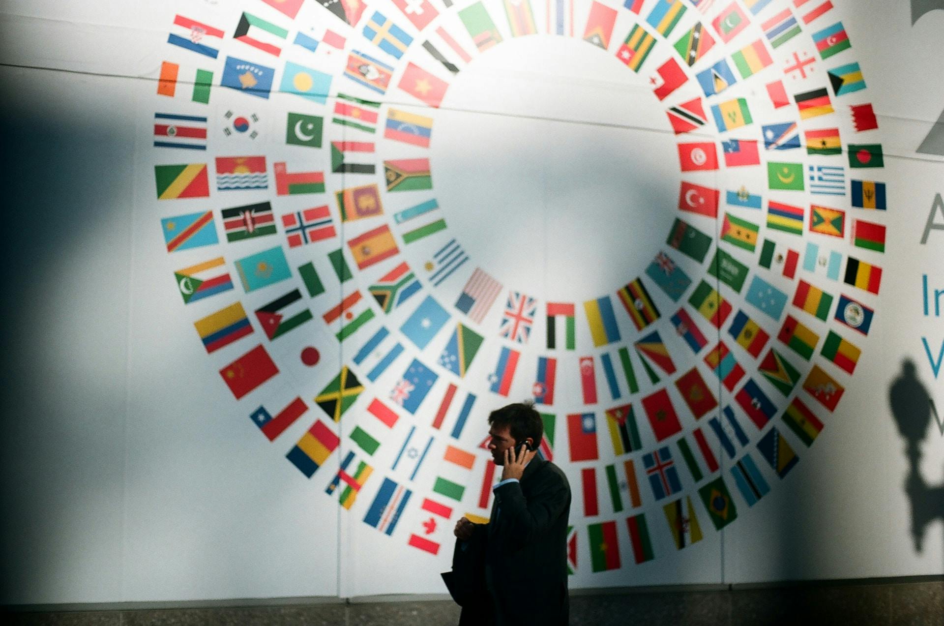 A person standing in front of a white wall with a lot of country flags positioned in a circle.