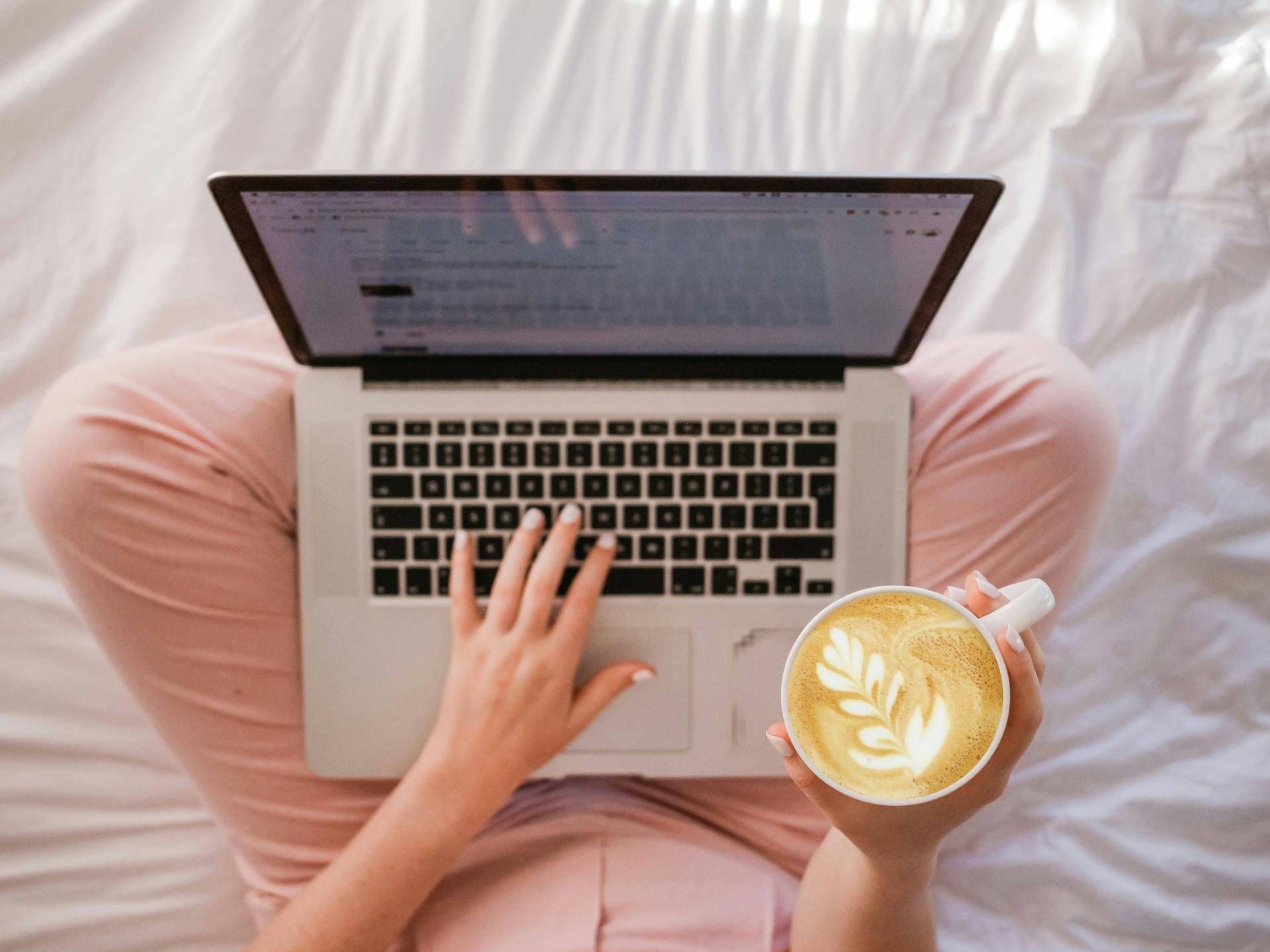 A person sitting in bed with a laptop computer and a coffee